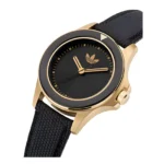 Auksinis ir juodas „Adidas“ laikrodis, pasižymintis elegantišku, minimalistiniu dizainu su subtiliu logotipu ant ciferblato ir tekstūriniu juodu dirželiu.