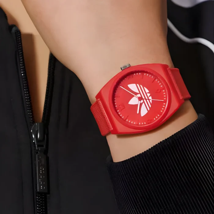 Stambiu planu matomas raudonas rankinis laikrodis su ryškiu logotipu, nešiojamas ant žmogaus rankos ir derinamas su juoda striuke su užtrauktuku.