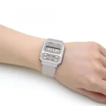 Skaitmeninio „Casio“ laikrodžio, rodančio 11:57:10, nešiojamo ant žmogaus riešo, stambiu planu baltame fone.