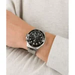 A close-up of a silver watch with a black dial and chronograph features on a wrist, paired with a gray sweatshirt.