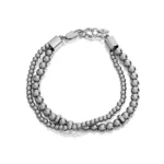 Stilinga dviguba apyrankė su blizgiais metaliniais karoliukais, sujungta elegantiškais užsegimais ir grandinės detalėmis.