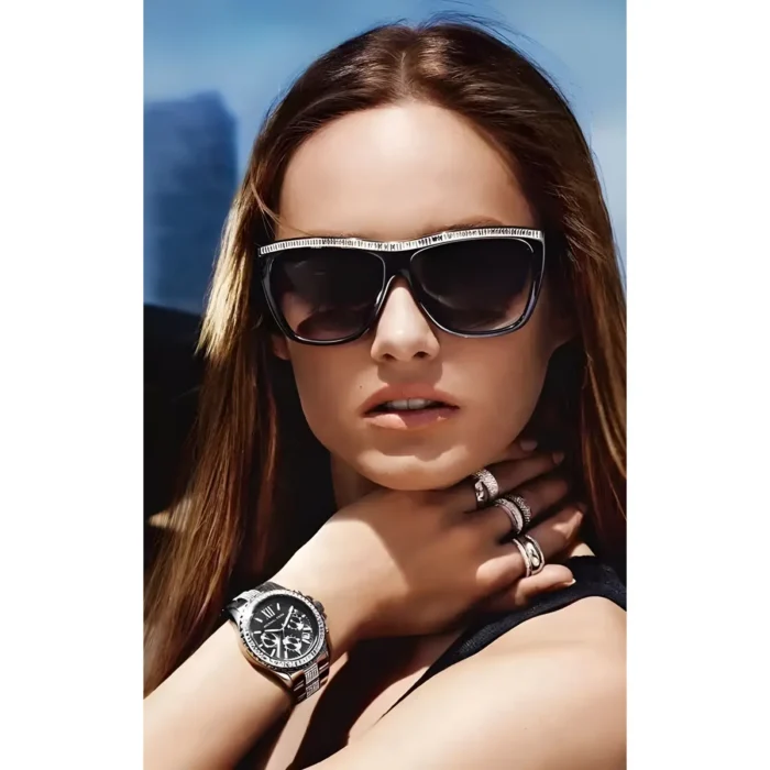 MICHAEL KORS MK5829-3 Persona ar gariem brūniem matiem valkā vairākus gredzenus un stilīgu melnu pulksteni, pozējot uz ainaviska fona.