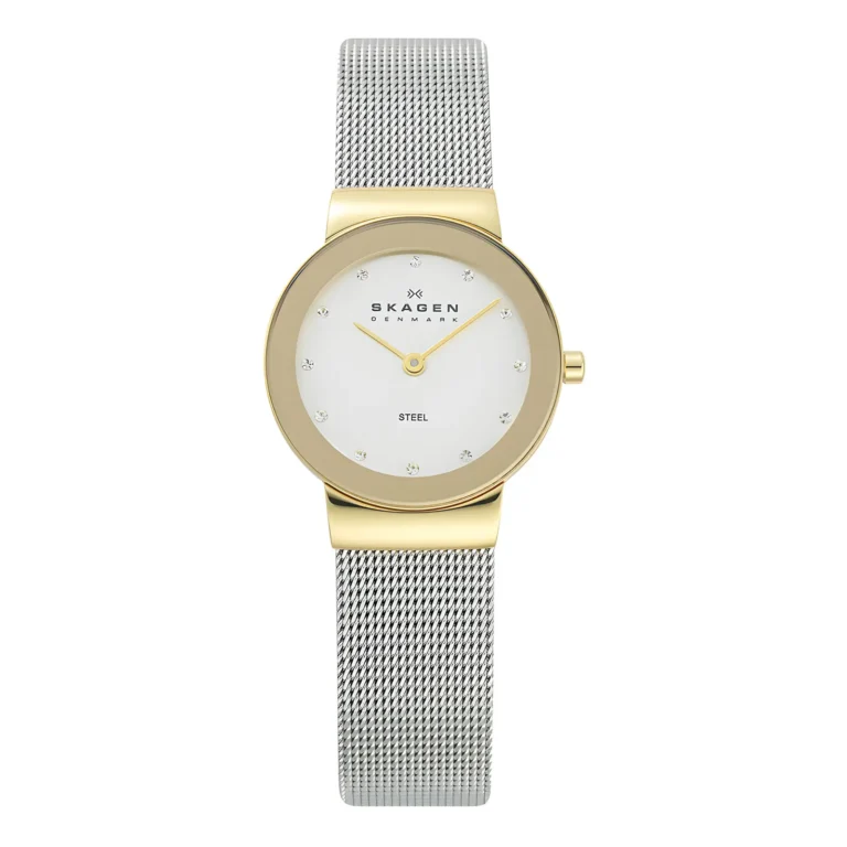 Stilingas „Skagen“ laikrodis su aukso spalvos korpusu, baltu ciferblatu su krištolo žymekliais ir sidabro spalvos tinkliniu dirželiu. Elegantiškas ir modernus dizainas.