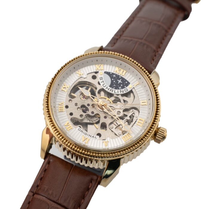 Elegant Stuhrling-klocka med skeletturtavla, detaljer i guldton och brunt läderarmband. Har intrikata kugghjul och romerska siffror.