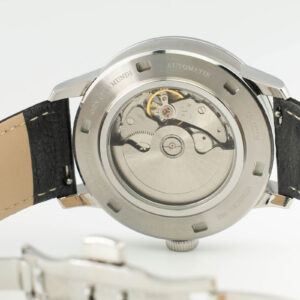 Närbild av baksidan på en automatisk klocka i rostfritt stål, som visar intrikata mekaniska rörelser och ett läderarmband.