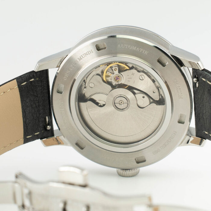 Nerūdijančio plieno automatinio laikrodžio nugarėlė, kurioje matomas sudėtingas mechaninis mechanizmas ir odinis dirželis.