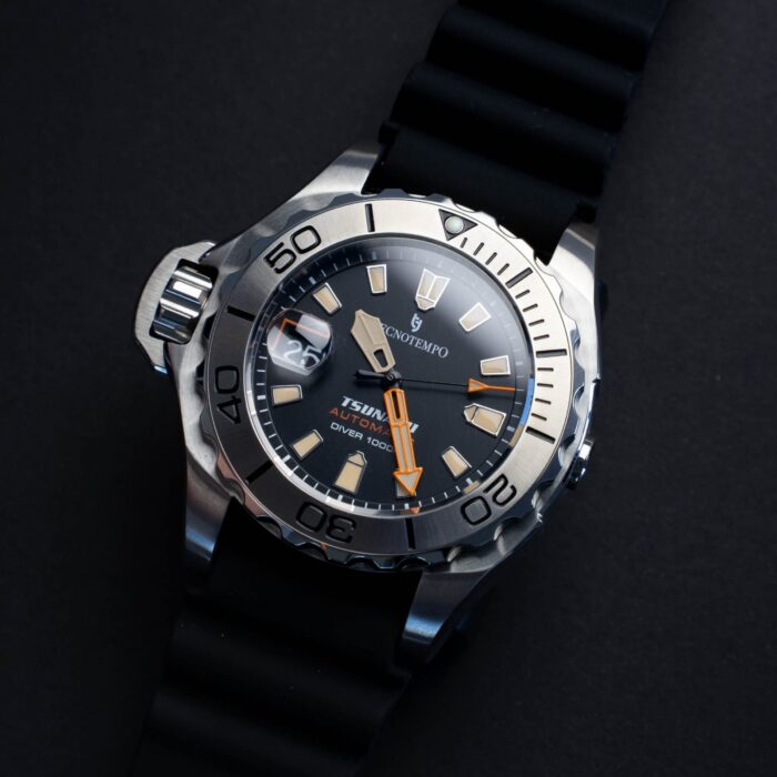 Lähikuva kestävästä sukeltajakellosta, jossa metallikuori, musta kumihihna ja tumma kellotaulu, jossa hehkuvat merkit ja oranssit yksityiskohdat.