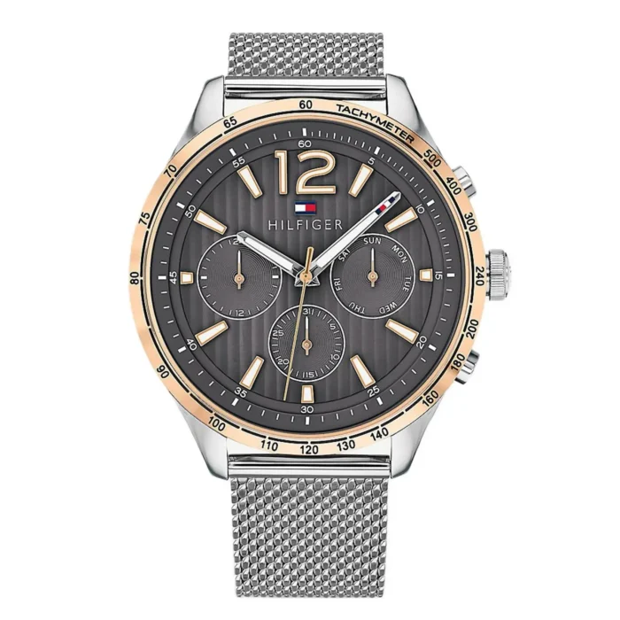 Vyriškas Tommy Hilfiger riešinis laikrodis su tamsiai pilku ciferblatu, auksinėmis detalėmis ir sidabriniu tinkleliu dirželiu. Stilingas pasirinkimas su tachimetru ir dienos/datų funkcijomis.