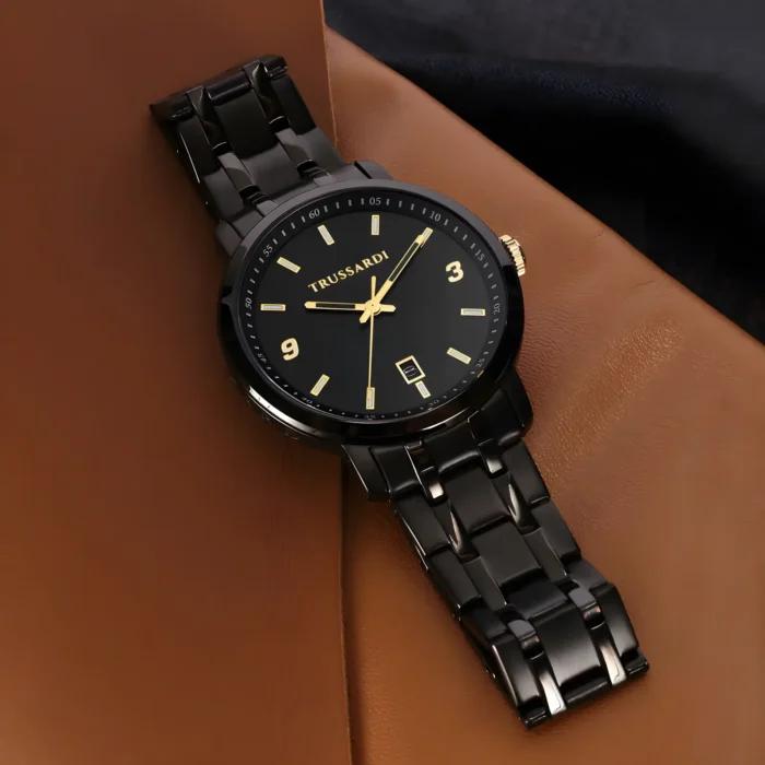 TRUSSARDI R2453147009-5 A sleek black Trussardi watch with a gold accent and a date function, resting on a brown leather surface.