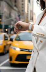 A woman in a white blazer checks her watch on a busy city street, with yellow taxis blurred in the background, conveying a sense of urgency and urban life.