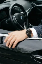 Man wearing a black watch rests his hand on the open window of a black BMW. The interior is partly visible, conveying a sense of luxury and style.