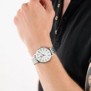 A close-up of a person's wrist wearing a stylish silver watch with a white face and blue hands, against a plain background.