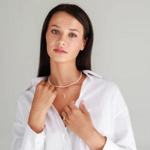 A woman in a white shirt showcases a pearl necklace and rings, exuding elegance with subtly styled accessories.