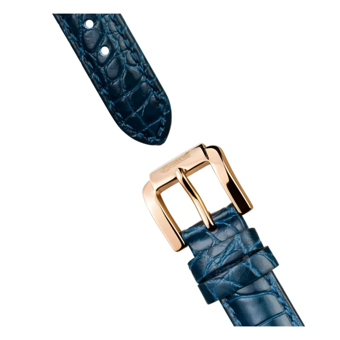 Close-up of a blue crocodile leather watch strap with a gold-tone rectangular buckle and two adjustment holes.