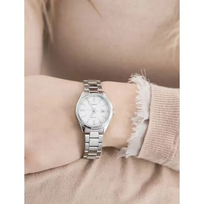 A close-up of a silver Casio watch on a woman's wrist, paired with a beige sweater, showcasing its elegant face and bracelet design.