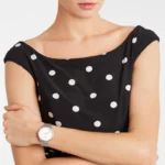 A woman in a polka dot dress with bare shoulders, showing a stylish watch on her wrist, exudes elegance and confidence.