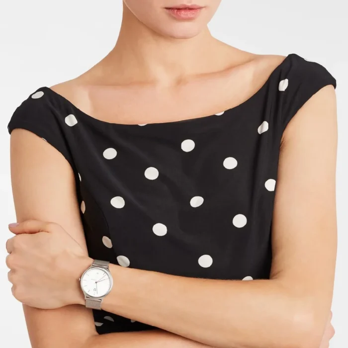A woman in a polka dot dress with bare shoulders, showing a stylish watch on her wrist, exudes elegance and confidence.
