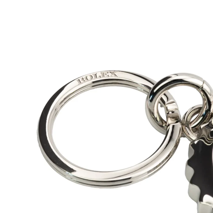 Close-up of a shiny, silver Rolex keyring featuring the engraved logo and a decorative charm