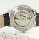 Close-up of a stainless steel automatic watch back, showcasing intricate mechanical movement and a leather strap.