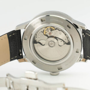 Close-up of a stainless steel automatic watch back, showcasing intricate mechanical movement and a leather strap.