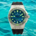 Крупный план часов Tecnotempo Ocean Force с синим циферблатом, люминесцентными метками и черным резиновым ремешком на фоне яркого океанского пейзажа.