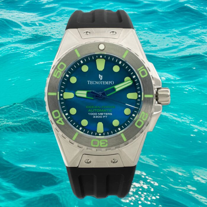 Крупный план часов Tecnotempo Ocean Force с синим циферблатом, люминесцентными метками и черным резиновым ремешком на фоне яркого океанского пейзажа.