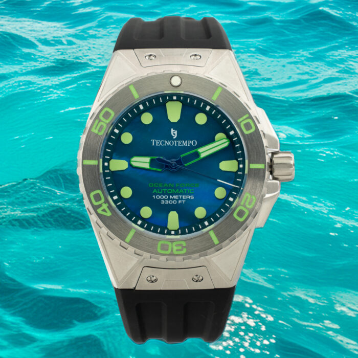 Laikrodžio „Tecnotempo Ocean Force“ su mėlynu ciferblatu, šviečiančiais žymekliais ir juodu guminiu dirželiu ryškiame vandenyno fone stambiu planu.