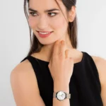A woman in a black sleeveless top shows off a stylish silver watch on her wrist while resting her finger on her chin.