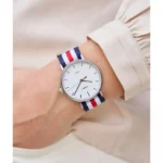 Close-up of a person's wrist wearing a minimalist white dial watch with navy, red, and white striped NATO strap.