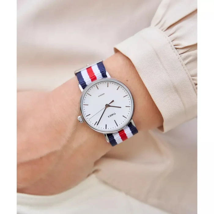 Close-up of a person's wrist wearing a minimalist white dial watch with navy, red, and white striped NATO strap.