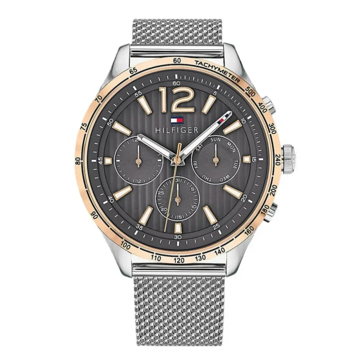 Men's Tommy Hilfiger wristwatch featuring a dark grey dial, gold accents, and a silver mesh strap. Stylish with a tachymeter and day/date functions.