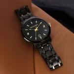 A sleek black Trussardi watch with a gold accent and a date function, resting on a brown leather surface.